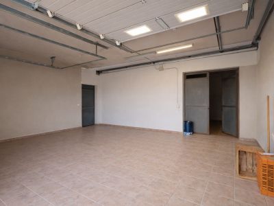 Spacious garage or utility room featuring light-tiled flooring, industrial ceiling lights, and multiple access points.