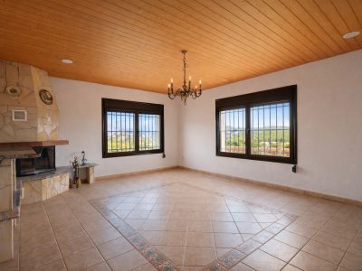 Spacious room featuring a stone-clad fireplace, a wooden plank ceiling, and a tiled floor with a decorative central pattern. Two barred windows offer valley views.