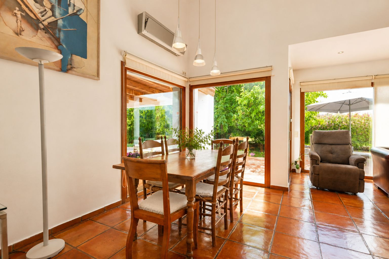 Sunlit main living room with handmade terracotta floors, a distinctive double-sided fireplace, and large windows, bathing the space in natural light and Mediterranean charm.