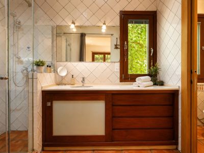 Bathroom featuring a glass shower, dark wood vanity with white countertop and integrated sink. A window offers green views, complemented by diamond-patterned white tiles and terracotta floors.