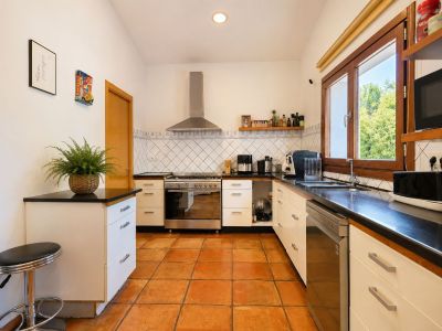 Functional kitchen featuring artisanal terracotta floors, dark countertops, and large wooden-framed windows providing abundant natural light.