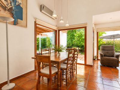 Sunlit main living room with handmade terracotta floors, a distinctive double-sided fireplace, and large windows, bathing the space in natural light and Mediterranean charm.