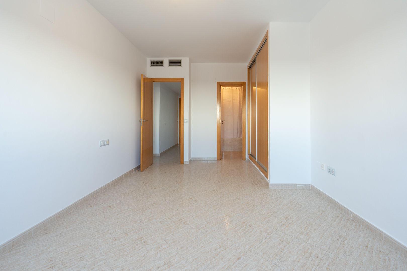 Empty room featuring light tiled flooring, a built-in wooden wardrobe with sliding doors, and multiple wooden doors leading to adjacent spaces. Air conditioning vents are visible.