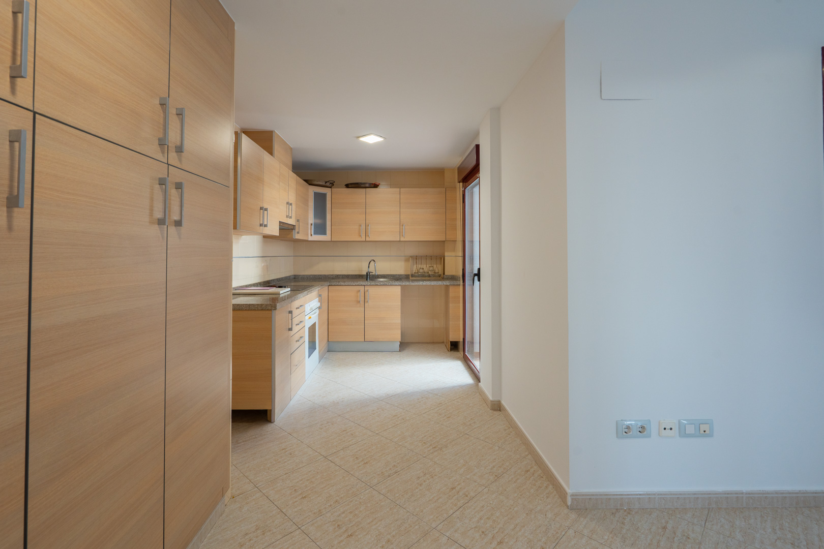 Equipped kitchen with light wood cabinetry, granite countertops, and tiled flooring. Features a glass door leading to a patio.