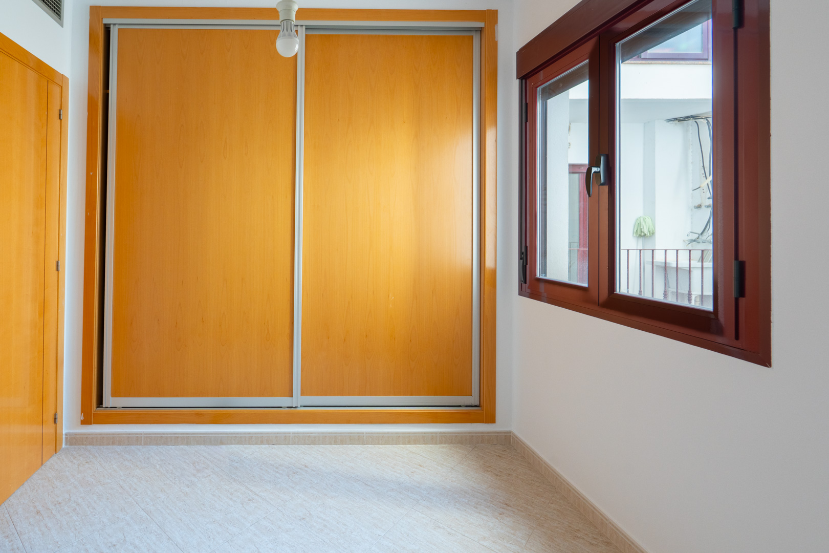 Secondary bedroom featuring a large built-in wardrobe with light wood sliding doors and a dark wood-framed window overlooking an interior patio.