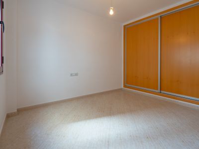 Bright room featuring a built-in wardrobe with two light wood sliding doors and a beige tiled floor. A window with a dark frame provides natural light.