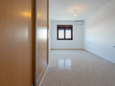 Empty room featuring a light wood built-in wardrobe, diagonally laid beige tiled floor, and a window with a corrugated roof view. Air conditioning unit visible.