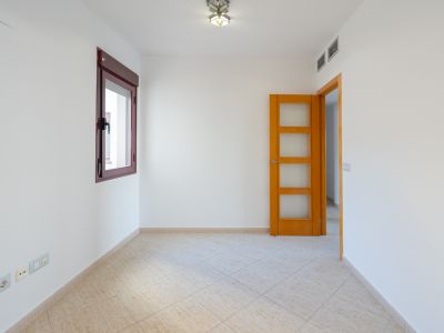 Empty room featuring white walls, a dark red-framed window, and light beige diagonal floor tiles. A wooden door with glass panels and AC vents are visible.