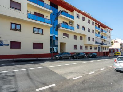 Exterior view of the residential building featuring a light facade, blue glass balconies, windows with maroon shutters, and a vertical glass panel.
