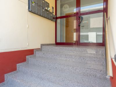 Granite-effect steps lead to the building's main entrance, featuring a dark red framed glass door etched with 'Edificio Alameda 36' and a row of grey mailboxes on the left wall.