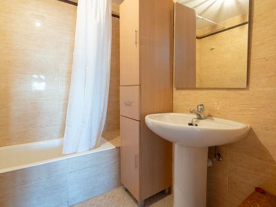 Second bathroom featuring a white pedestal sink, a tall wooden storage cabinet, and a bathtub with a shower curtain. Walls are finished with light beige tiles.