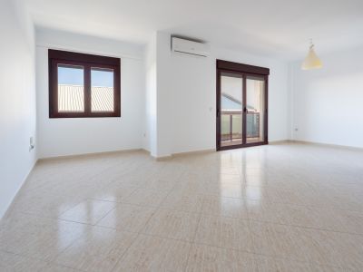 Spacious room featuring light beige tiled flooring, white walls, a window, and a sliding door with dark brown frames leading to a terrace. Includes a wall-mounted AC unit.