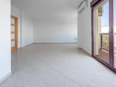 Spacious, unfurnished living-dining area with light tiled flooring, a wooden door with frosted glass panels, and access to a terrace via a dark red aluminum sliding door. An AC unit is visible.