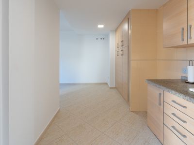 Transition from the kitchen, featuring granite countertop and light wood cabinets, to a hallway with beige ceramic floor and wall hooks.