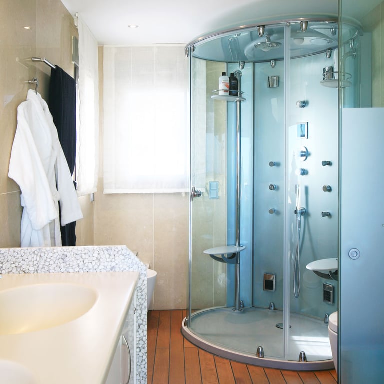 Bathroom featuring a multi-jet glass shower cabin, a vanity with a unique pebble-textured countertop, and warm wooden flooring. Natural light filters through the window.