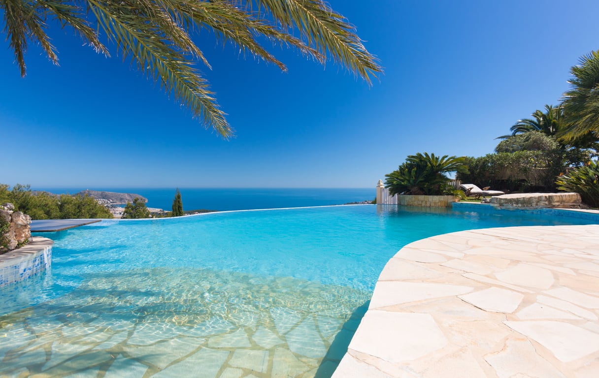 Infinity pool featuring a beach-style entry and light stone coping, providing panoramic views of the Mediterranean Sea and distant coastline.