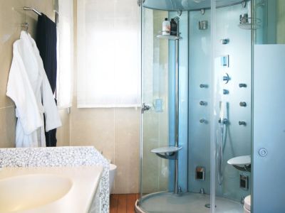 Bathroom featuring a multi-jet glass shower cabin, a vanity with a unique pebble-textured countertop, and warm wooden flooring. Natural light filters through the window.