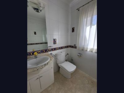 Bathroom featuring white tiled walls with a decorative border and rooster accents. Includes a sink with a light marble vanity, toilet, and window with sheer curtains.
