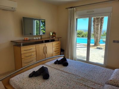 Bedroom featuring twin beds, a wall-mounted TV above a wooden dresser, and direct access to the outdoor terrace with a swimming pool and palm trees.