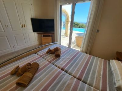 Bedroom featuring two single beds, a built-in wardrobe, and a wall-mounted TV. Direct access to the exterior pool area with archway and clear views.