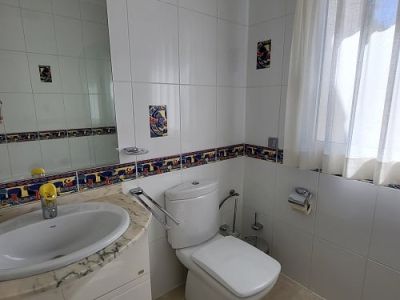 Bright bathroom featuring white wall tiles with a colorful decorative border and accent pieces. Includes a marble-topped vanity with integrated sink, a modern toilet, and a window with a sheer curtain.