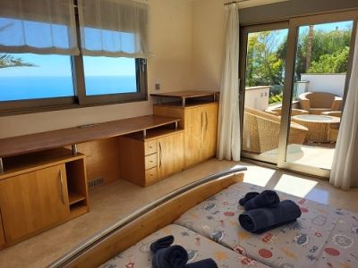 Bright bedroom featuring twin beds, an integrated wooden desk unit, and expansive sea views. Direct access to a private outdoor terrace with seating.