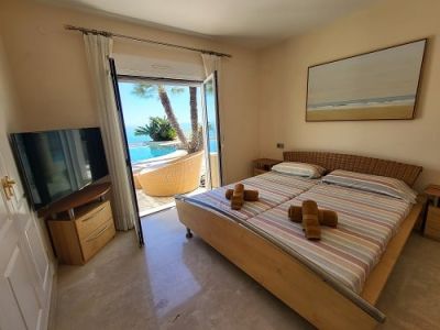 Bright bedroom with twin beds and a woven headboard, featuring direct access to the pool area and sea views. Includes a television and wall art.