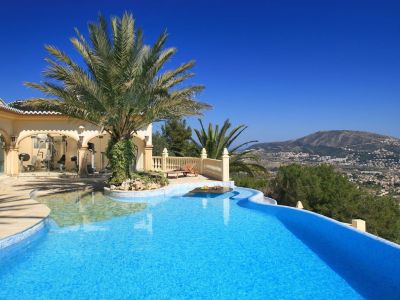 Curved mosaic pool with palm island and submerged table. Glass-enclosed gym and terrace offering panoramic mountain views.