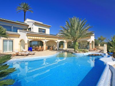 Expansive blue mosaic pool with beach-style entry, palm island, and in-water table. The villa features a covered naya and a glass-fronted gym.