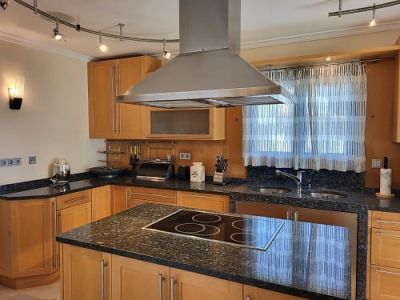 Functional kitchen featuring light wood cabinetry and dark granite countertops. A central island houses an induction hob beneath a stainless steel extractor hood.