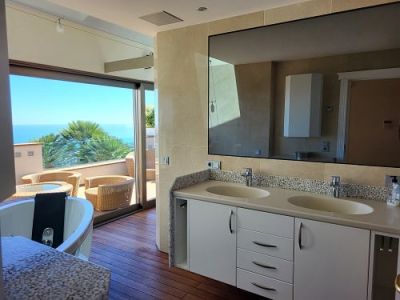 Master bathroom featuring a double vanity, a jetted tub, and direct access to a wooden terrace with wicker furniture and sea views.