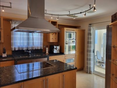 Modern kitchen featuring light wood cabinetry, dark granite countertops, an island with integrated hob, and stainless steel appliances. A glass door leads to an adjacent gym space.