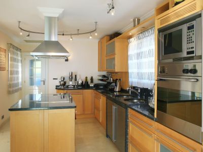 Modern kitchen featuring light wood cabinetry, dark granite countertops, and a central island with an integrated hob. Stainless steel appliances include a built-in oven, microwave, and extractor hood.