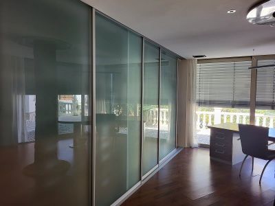 Office or bedroom featuring sleek frosted glass sliding doors, dark wood flooring, and a dedicated workspace by the window overlooking the balustrade.