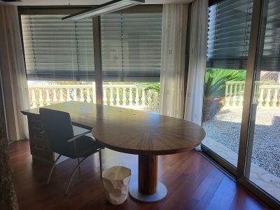 Spacious private office featuring a large wooden desk and hardwood floors. Floor-to-ceiling windows overlook a balustrade and Mediterranean garden.