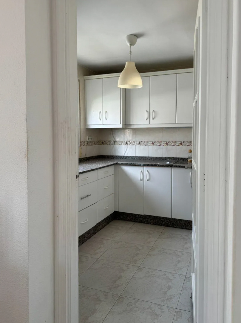 Compact kitchen featuring white cabinetry, dark speckled granite countertops, and a decorative tiled backsplash. The space is illuminated by a central pendant light and light floor tiles.