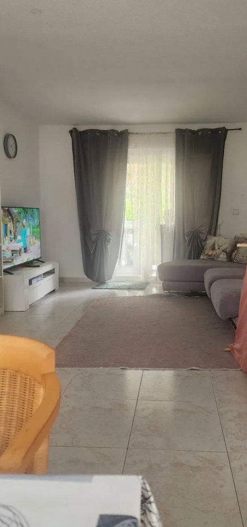 Spacious living room with natural light, featuring tiled floors, a comfortable sectional sofa, and direct access to a terrace through glass doors with elegant curtains.