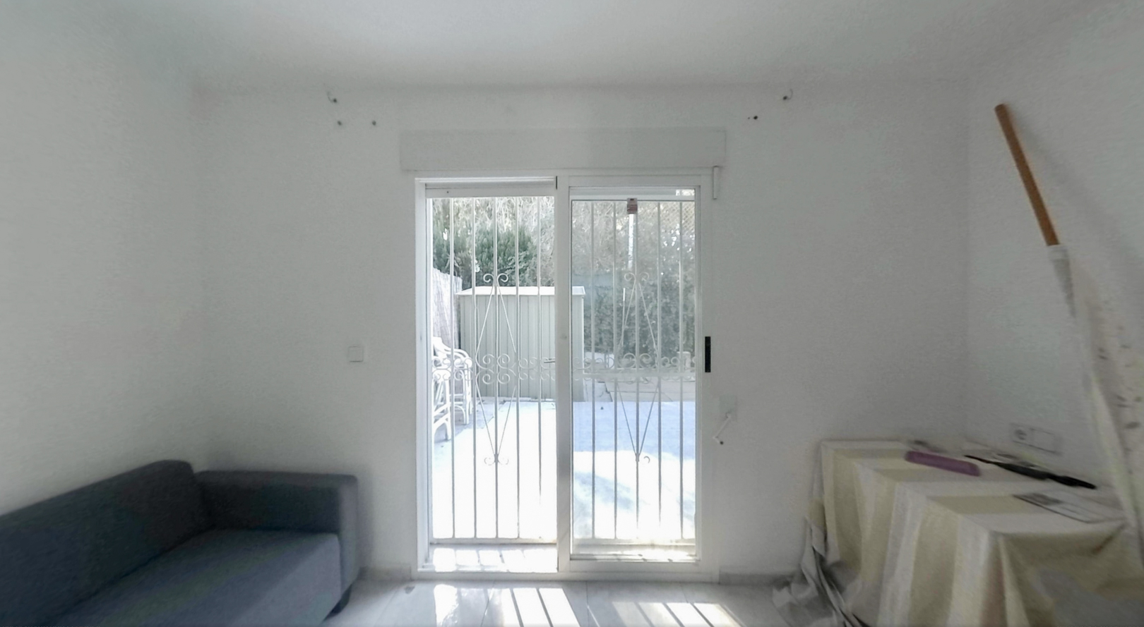 Spacious room with sliding glass doors and security bars, providing direct access to the private garden, illuminated by abundant natural light on the light-toned floor.