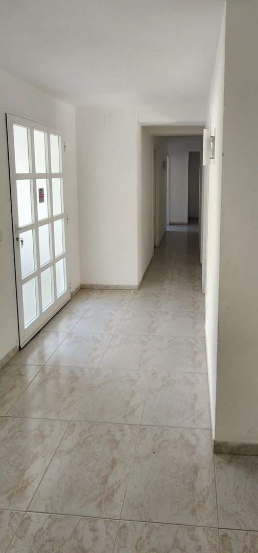 View of the main entrance hallway with light-toned tiled flooring, white walls, and a multi-paneled door. The corridor extends into the interior, illuminated by a wall sconce.