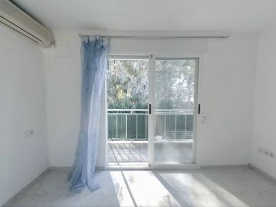 Bright bedroom featuring an air conditioning unit and direct access to a private terrace. Light tiled flooring and views of lush greenery.