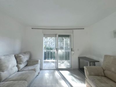 Bright living room featuring light-colored sofas, tiled flooring, and sliding glass doors that open to a balcony, allowing natural light to illuminate the space.