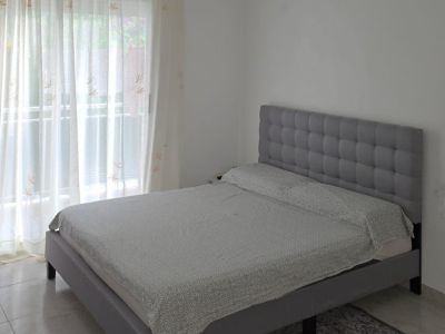 Double bedroom featuring a grey upholstered bed with a tufted headboard, tiled flooring, and ample natural light from the window with terrace access.
