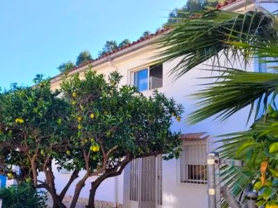 Exterior view of the white villa, featuring a tiled roof and citrus trees bearing yellow fruit. Ground-floor entrance and upper windows are visible.