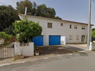 Front exterior of the semi-detached villa, featuring a white facade, two distinctive blue garage doors, and a mature orange tree by the wrought-iron entrance gate.