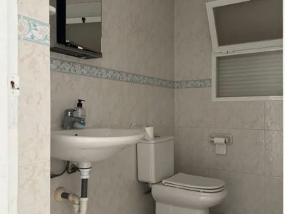 Functional bathroom featuring light-toned tiles, a decorative border, and an open top-hinged window. Equipped with a wall-mounted sink, toilet, and mirrored cabinet with light.