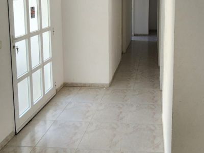 Interior hallway featuring light-toned tiled flooring and white walls. A white door with frosted glass panels is on the left, leading to a long corridor illuminated by a wall sconce.