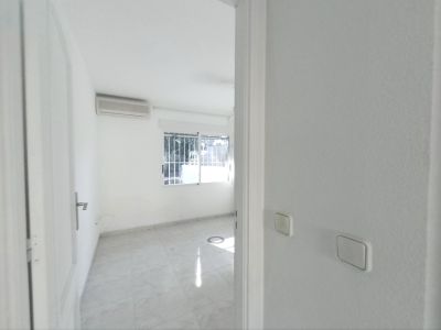 View into an unfurnished room featuring light tiled flooring, white walls, and an air conditioning unit. A window with security bars provides natural light.
