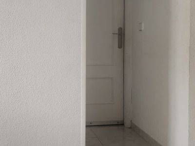 View of a bright hallway with light-colored tiled flooring and white textured walls. A decorative cherub ornament adorns the left wall, leading to a white door with a silver handle.