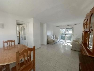 View of the bright living-dining area featuring an oval wooden table, tiled floors, and a large wooden display cabinet. Sliding glass doors open to a balcony, filling the space with natural light.