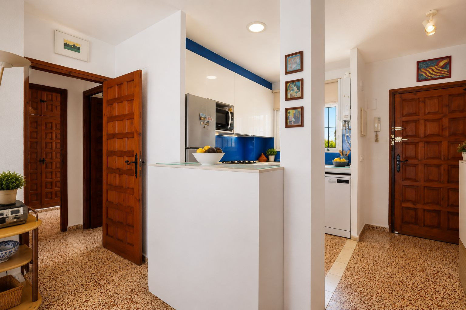 The entrance hallway showcases unique patterned floor tiles and classic wooden doors. A modern kitchen with a blue backsplash and white units is visible, separated by a functional half-wall.
